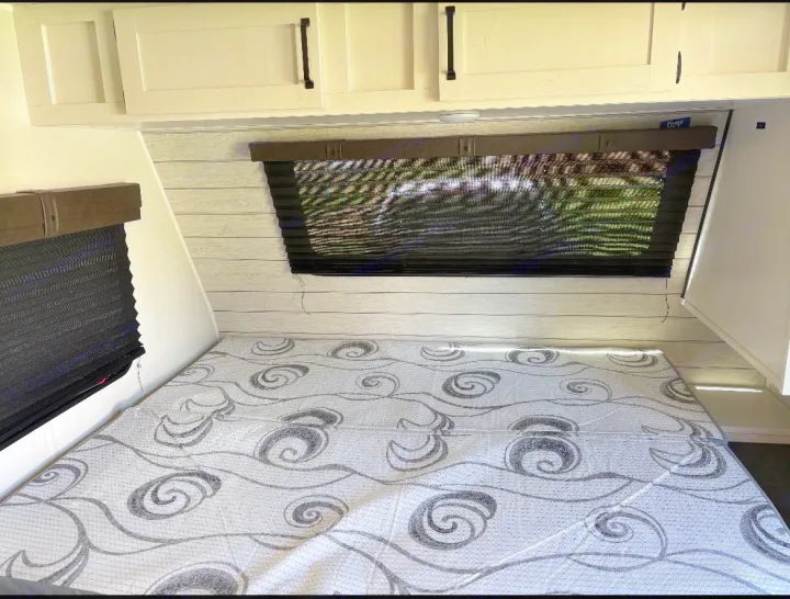 RV rental bedroom: a comfortable sleeping area with patterned mattress, wood-paneled walls, overhead cabinets, and dark blinds.. Puma Palomino 2024