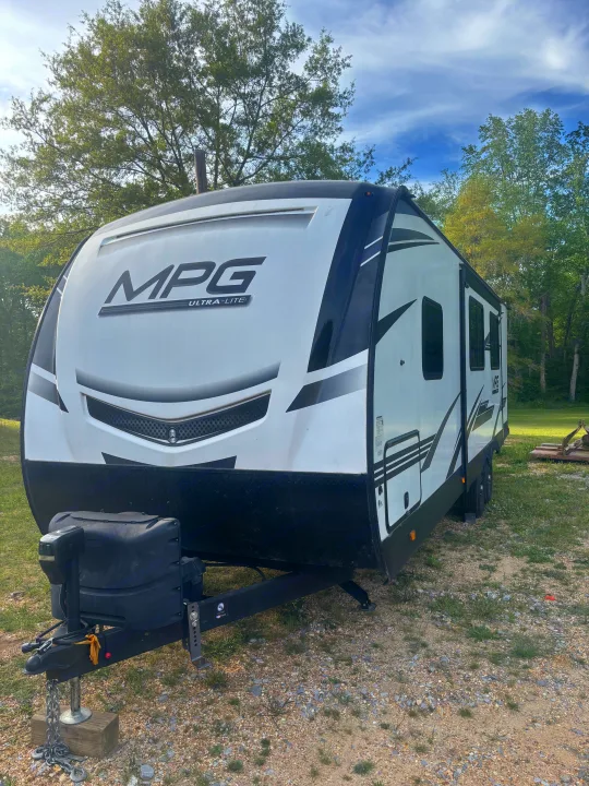 This white & black travel trailer RV rental, an MPG Ultra-Lite model, is parked on gravel under trees, ready for your next adventure.. Cruiser RV MPG 2022
