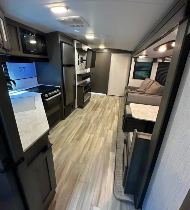 Explore this modern RV rental interior featuring a spacious kitchen with a microwave & stove, dining booth, and comfortable living area with a sofa.. Cruiser RV MPG 2022