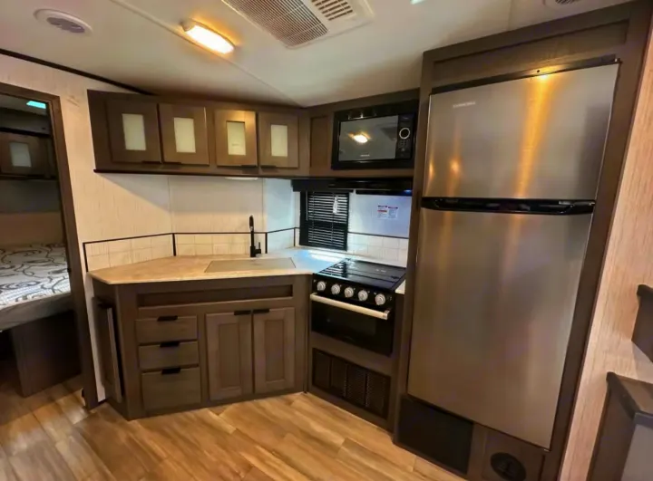 This modern RV rental kitchen features a stainless fridge, microwave, stove, sink, and ample storage, perfect for travel.. Cruiser RV MPG 2022