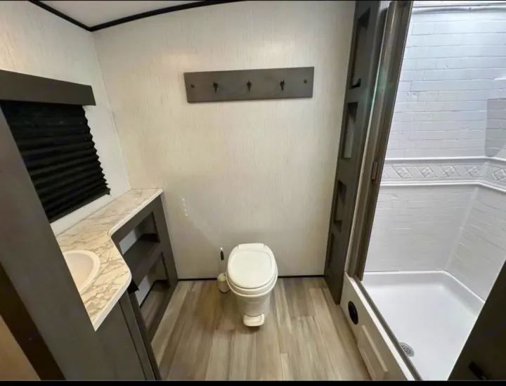 Compact RV rental bathroom with a toilet, sink in a vanity, and a shower stall. Features light textured walls and wood-look flooring.. Cruiser RV MPG 2022