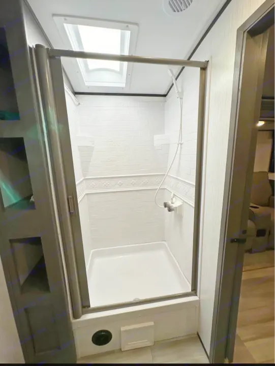 Modern RV rental shower featuring white tile-look walls, clear door, skylight, and handheld shower. Ready for your adventure.. Cruiser RV MPG 2022