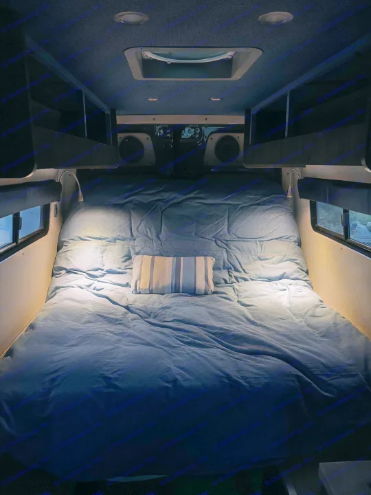 This RV rental's cozy bed features denim-blue bedding, a striped pillow, and bright reading lights for comfortable travels.. Mercedes Sprinter 2020