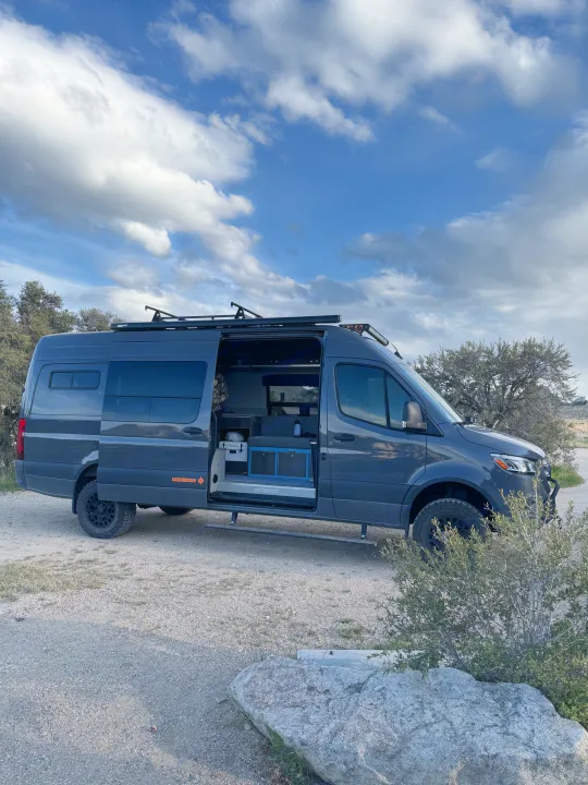 Adventure-ready custom Mercedes Sprinter camper van for rv rental, parked outdoors. Open door shows interior.. Mercedes Sprinter 2020