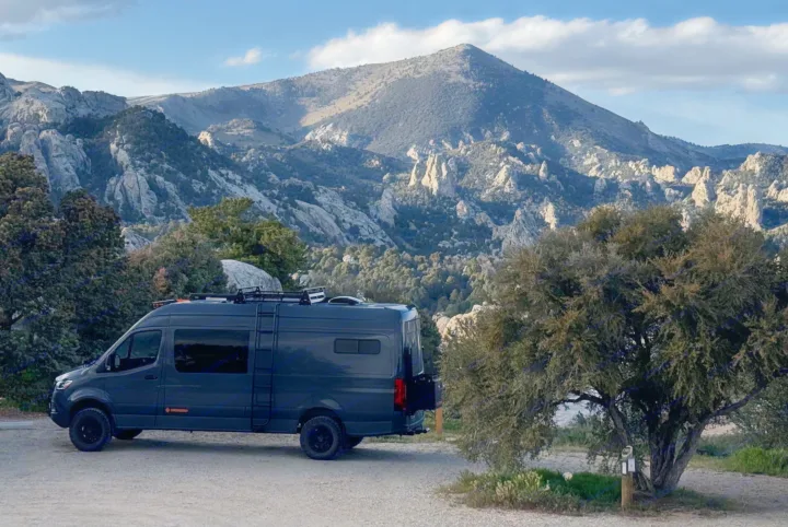 This dark camper van RV rental is ready for adventure! Parked in a stunning mountainous landscape with rocky peaks & trees.. Mercedes Sprinter 2020