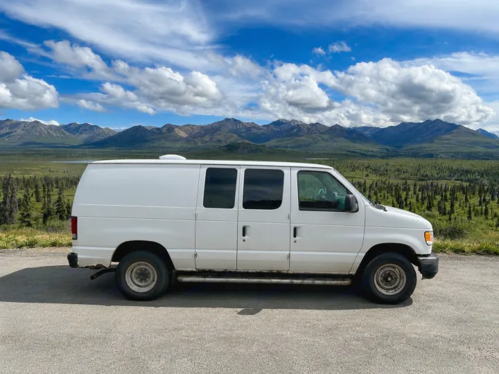 White camper van parked on a scenic road with majestic mountains & a lush valley. Your next RV rental adventure awaits!. Ford Econolline 250s 2013