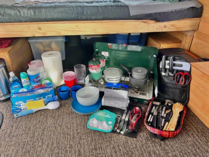 RV rental ready: Camp stove, pots, dishes, and cleaning supplies neatly organized under a bed for mobile cooking.. Ford Econolline 250s 2013