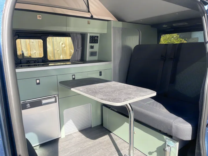 Inside a modern RV rental: kitchenette with fridge, dining table, bench seat, and pop-top roof for your travels.. Ford Transit Custom 2+2 berth Pop Top, Automatic 2026