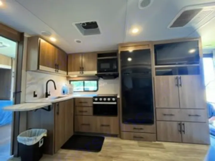 Modern RV rental kitchen interior: large fridge, microwave, stove, sink, ample wood-grain cabinets, and TV for comfortable travels.. Grand Design Imagine 2022