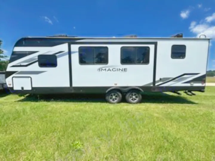 White Imagine travel trailer RV rental, featuring black graphics and dual axles, parked on grass for your next adventure.. Grand Design Imagine 2022