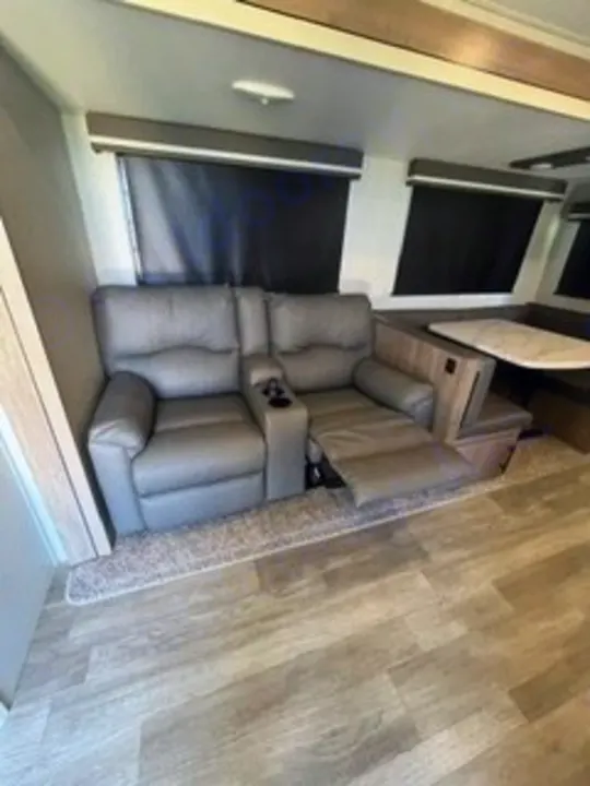 Comfortable RV rental interior: recliners with cup holders, extended footrest, and a dining area with bench seating.. Grand Design Imagine 2022