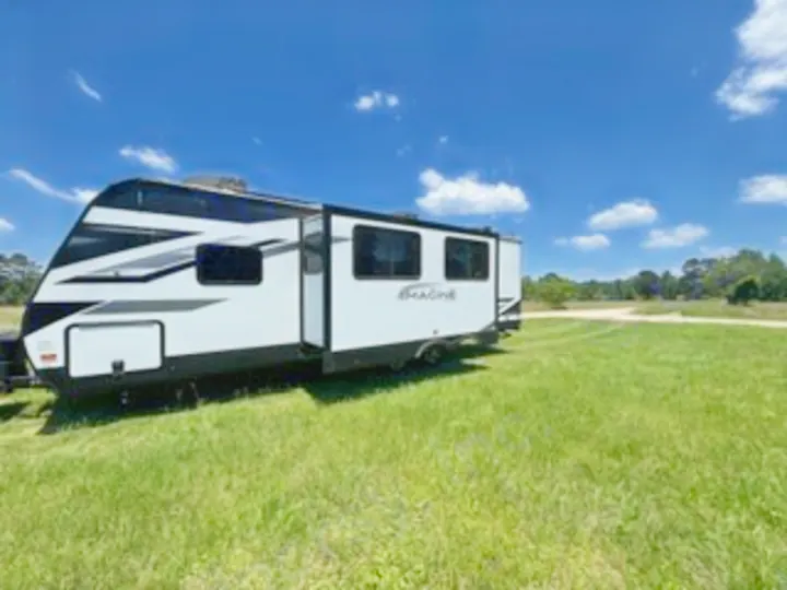 RV rental: A sleek white travel trailer with an extended slide-out, parked in a sunny grassy field, ready for adventure.. Grand Design Imagine 2022