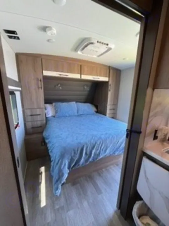 Spacious RV rental bedroom with a queen bed, overhead storage, and AC unit for your comfortable travel adventures.. Grand Design Imagine 2022