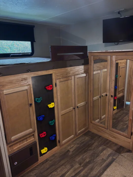 Experience an RV rental! This image shows a bunk bed with a colorful climbing wall ladder, storage cabinets, and a wall-mounted TV.. Coachmen Freedom Liberty Express 2018