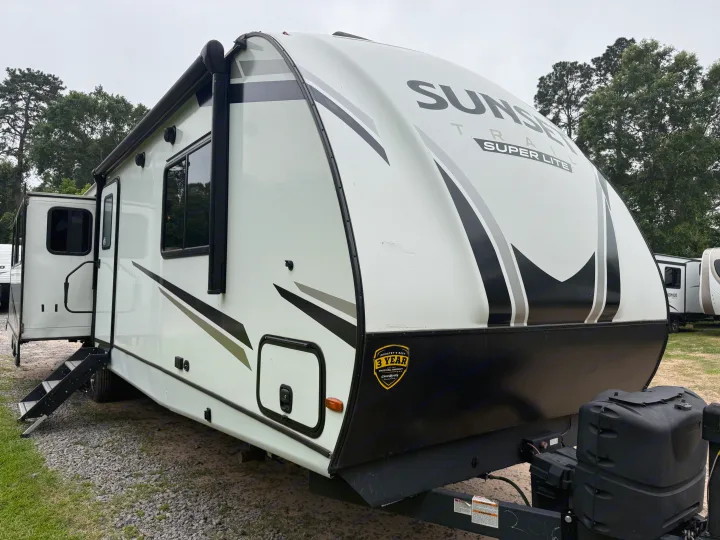 Front-left view of a white and black Sunset Trail Super Lite RV rental, steps extended on a gravel lot under an overcast sky.. Crossroads RV Sunset Trail Super Lite 2022