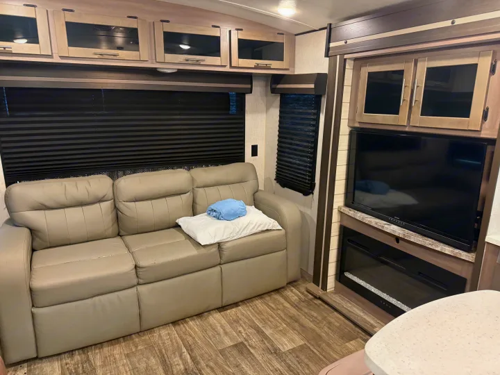 Cozy RV rental living room features a comfy sofa, TV, electric fireplace, and overhead cabinets with pleated blinds.. Crossroads RV Sunset Trail Super Lite 2022