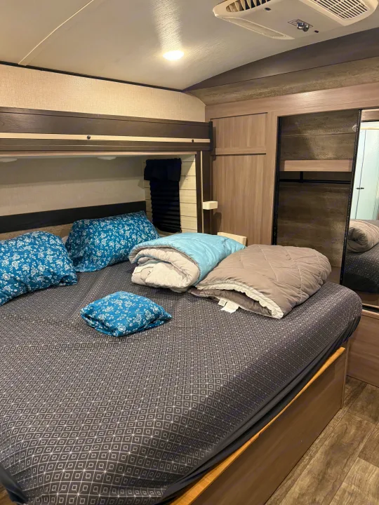 Cozy RV rental bedroom with patterned bed, blue pillows, rolled comforters, storage, and mirror.. Crossroads RV Sunset Trail Super Lite 2022