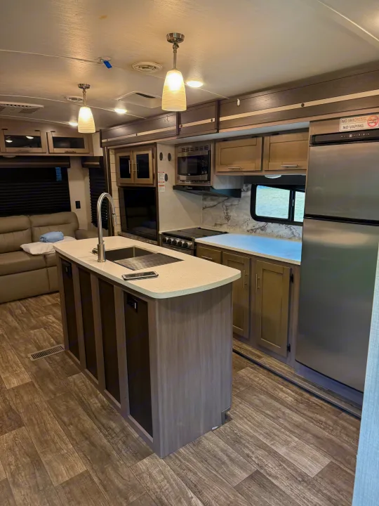 Modern rv rental kitchen with an island, sink, full appliances, and a living area, perfect for comfortable travel.. Crossroads RV Sunset Trail Super Lite 2022