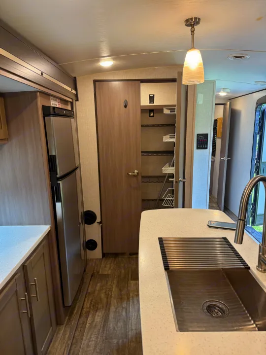 Spacious RV rental kitchen featuring a stainless steel fridge, organized pantry, sink with faucet, and modern cabinetry.. Crossroads RV Sunset Trail Super Lite 2022