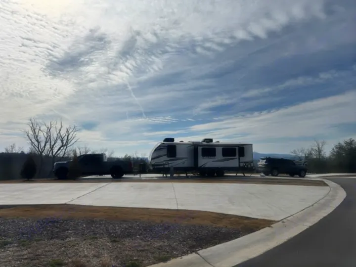 An RV rental travel trailer parked with a pickup truck and SUV at a modern campground site under a cloudy sky.. Keystone RV Bullet Premier Ultra Lite 2022