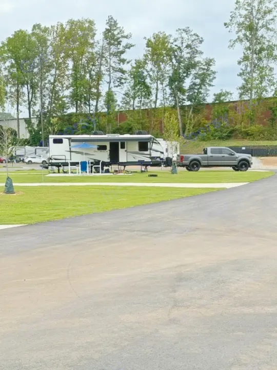 An RV rental travel trailer and gray pickup truck are parked at a spacious campground site with green grass and trees.. Keystone RV Bullet Premier Ultra Lite 2022