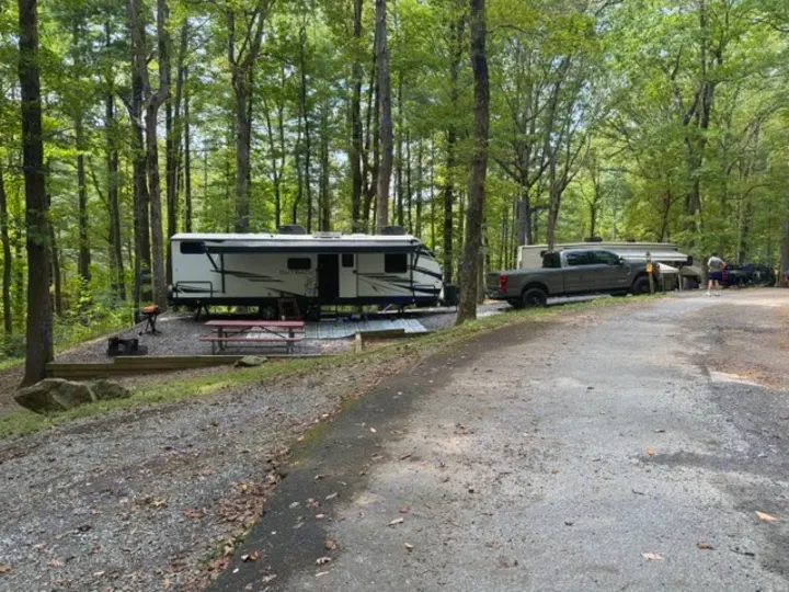 An rv rental parked at a serene wooded campsite, complete with a truck, picnic table, and grill, for an outdoor adventure.. Keystone RV Bullet Premier Ultra Lite 2022
