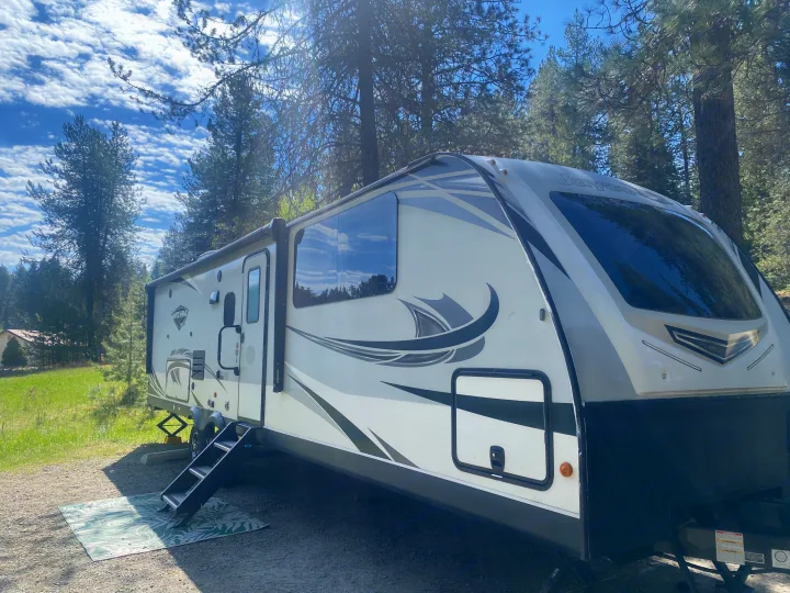 RV rental: This travel trailer is set up for camping among tall pine trees under a bright, cloudy sky, perfect for outdoor living.. Jayco White Hawk 2020