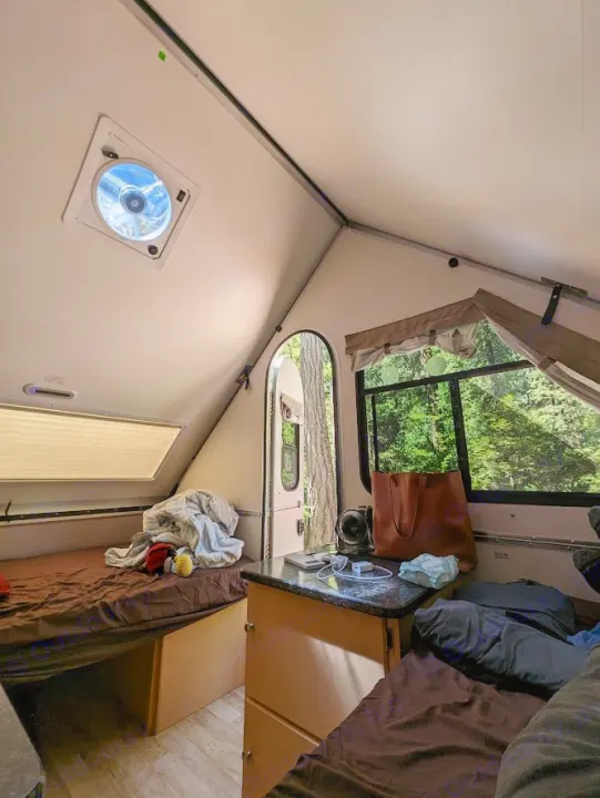 Inside a cozy rv rental bedroom with dual beds, storage, and a scenic nature view from the windows.. A Liner A Liner Popup Trailer 2022