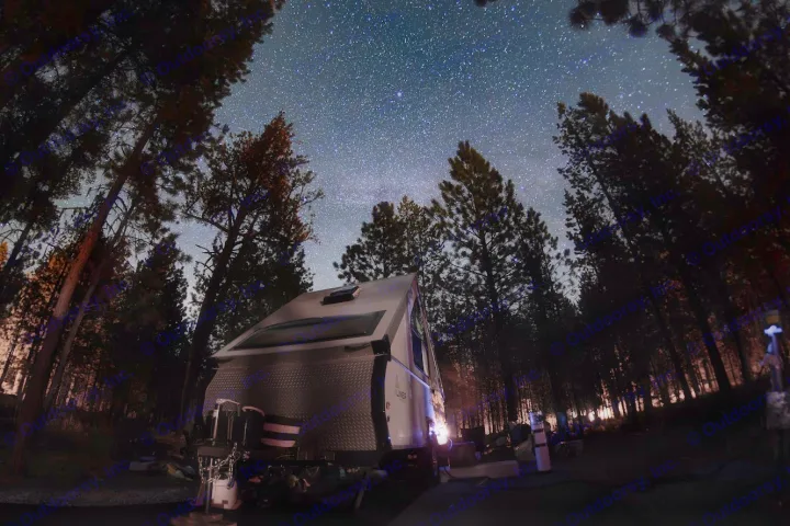 Stargazing from an RV rental campsite. An RV sits under a brilliant, star-filled Milky Way in a dark pine forest.. A Liner A Liner Popup Trailer 2022