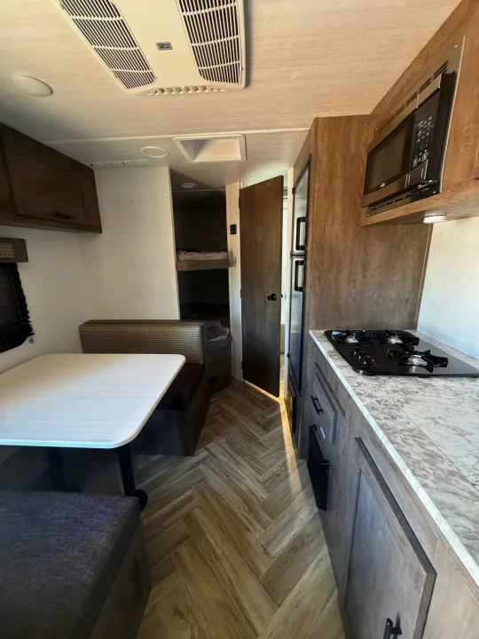 Explore this modern RV rental interior featuring a dining area, kitchen with stove/microwave, and convenient bunk beds.. Forest River Salem Select 2021