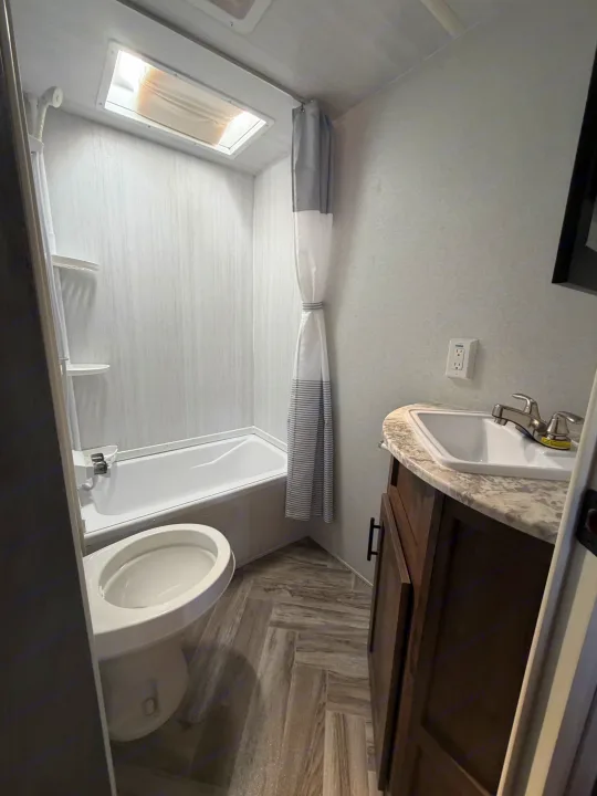 Clean RV rental bathroom featuring a tub/shower combo, toilet, and sink vanity with a skylight for natural light.. Forest River Salem Select 2021