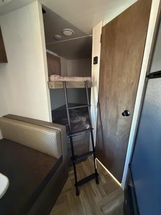 RV rental interior: bunk beds with ladder, adjacent dining booth, and door on right. Compact, functional living space.. Forest River Salem Select 2021