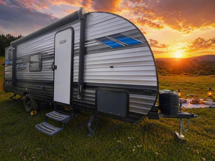 Experience an RV rental adventure! This travel trailer is set in a scenic field at sunset, with a cozy picnic blanket and lanterns nearby.. Forest River Salem Select 2021