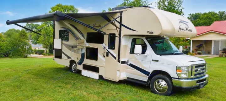 Tan and white Thor Four Winds Class C RV rental with extended awning on a green lawn, perfect for your next road trip.. Thor Four Winds 2018