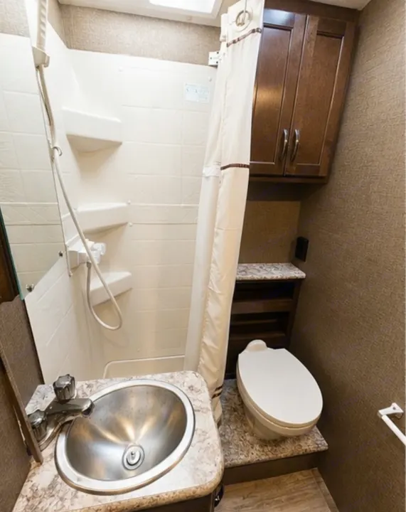 RV rental bathroom with a compact sink, stand-up shower, toilet, and wood storage cabinets for convenience on the go.. Thor Four Winds 2018