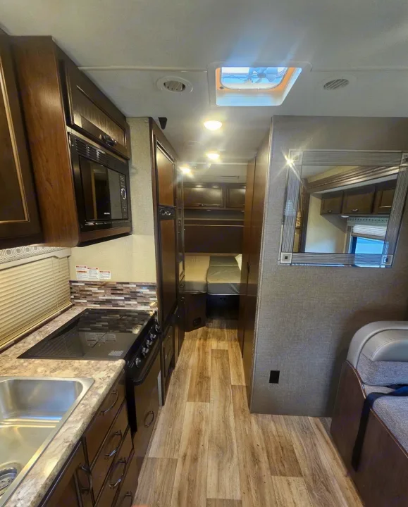 Inside an RV rental: kitchen with sink & stove, hallway to bed, and comfy seating.. Thor Four Winds 2018