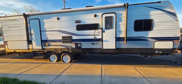 Explore the outdoors with this Springdale travel trailer RV rental, featuring a large awning, parked in warm sunlight.. Keystone RV Springdale 2021