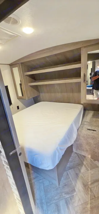 Cozy RV rental bedroom features a white bed, overhead shelves, mirrored cabinets, mixed flooring, ceiling lights, and AC vent.. Keystone RV Springdale 2021