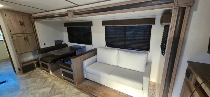 Interior of an RV rental showing a dinette with dark benches, a white sofa, and closed window blinds in a cozy living area.. Keystone RV Springdale 2021