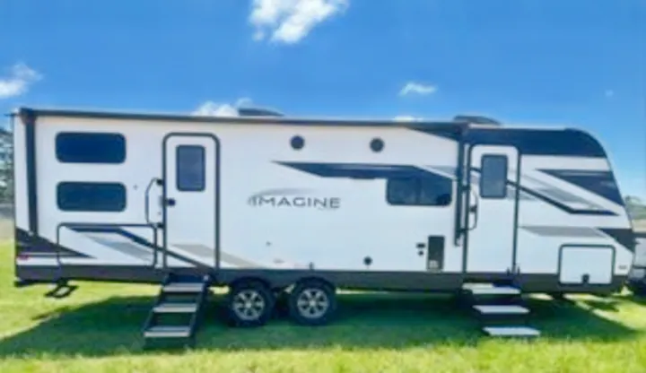 This modern white & black Imagine travel trailer is perfect for an RV rental. Parked on green grass with dual doors.. Grand Design Imagine 2022