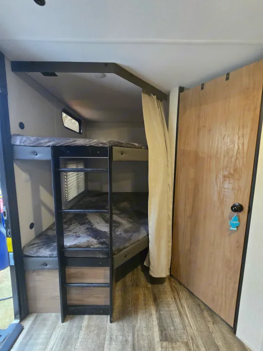 RV rental bunk bed interior with a ladder, privacy curtain, small window, and a light wood door.. Forest River Cherokee Grey Wolf 2024
