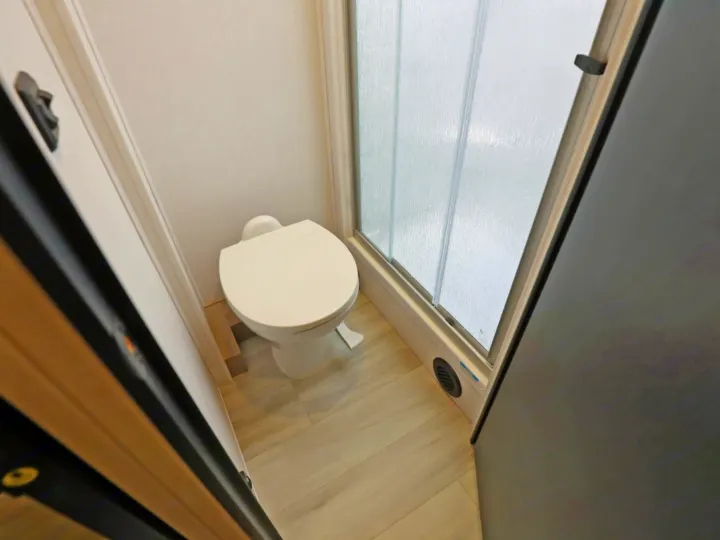 Inside an RV rental, this compact bathroom features a white toilet & an efficient frosted glass shower.. Classe C 24-26 pieds avec extension(s) 2027