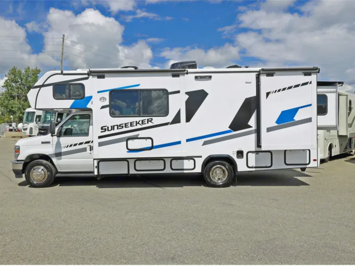 White Sunseeker Class C RV rental with blue and black graphics parked on asphalt, its side slide-out extended.. Classe C 24-26 pieds avec extension(s) 2027