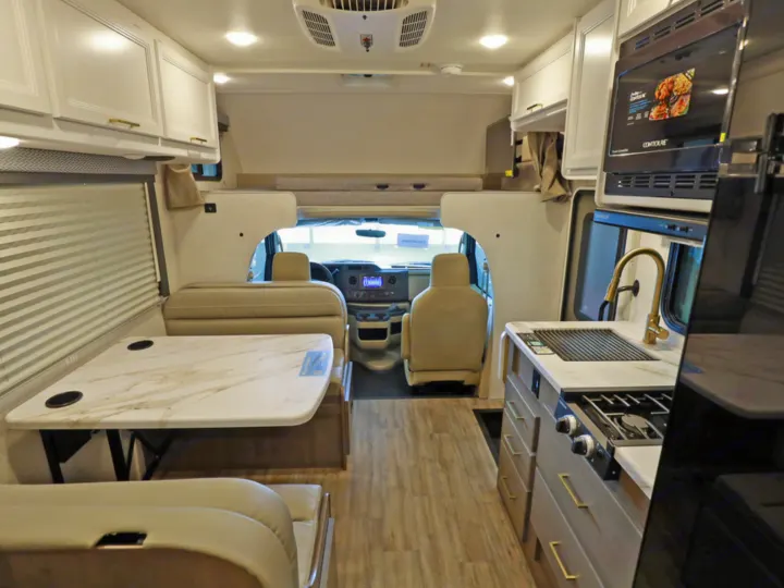 Modern RV rental interior showcasing a full kitchen, dining area, and cockpit. White cabinets, wood flooring, and comfortable seating.. Classe C 24'' sans extension Spare 2026