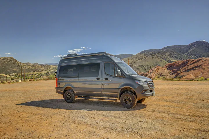 Off-road RV rental: A rugged Mercedes Sprinter adventure van in a scenic mountain landscape with red rocks, parked on a dirt lot.. Thor Tranquility 2025