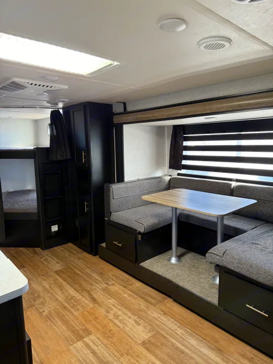 RV rental interior: a dinette with gray seating, bunk beds, dark cabinetry, and wood-look flooring. Perfect for your next trip.. Forest River Cherokee Grey Wolf 2022