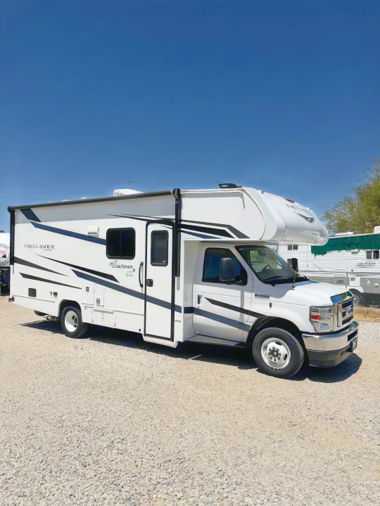 A white Coachmen Freelander Class C RV rental with black stripes, parked on a gravel lot under a clear blue sky.. Forest River Coachmen Freelander 2023