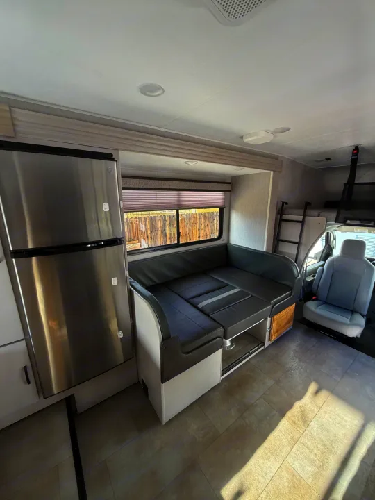 Spacious RV rental interior with a gray dinette, stainless steel refrigerator, and bunk bed. Tiled floor with natural light.. Forest River Coachmen Freelander 2023