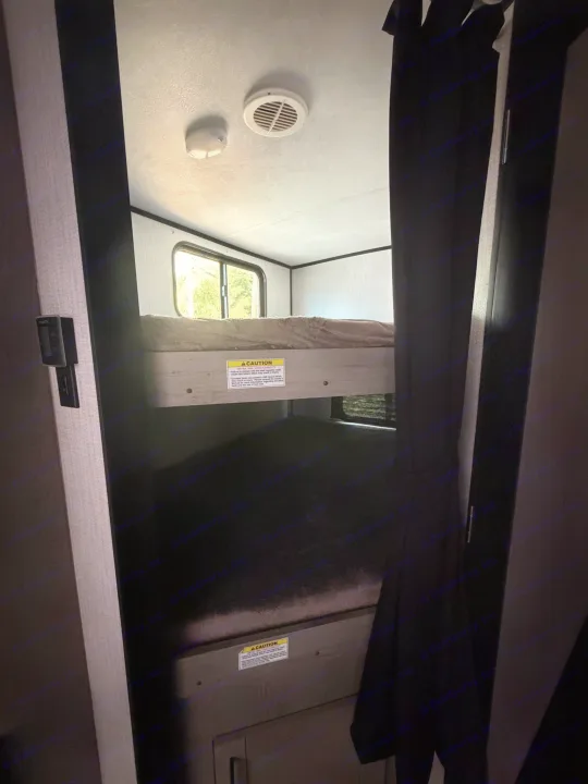 Cozy rv rental interior featuring stacked bunk beds with a window, ceiling light, and vent. Caution labels visible on bed frames.. Heartland RVs Mallard 2021