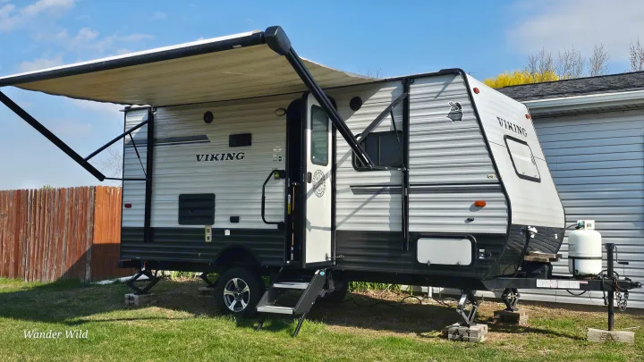A gray & black Viking travel trailer with an extended awning & steps down, parked on grass, ready for an rv rental adventure.. Forest River Viking 2018